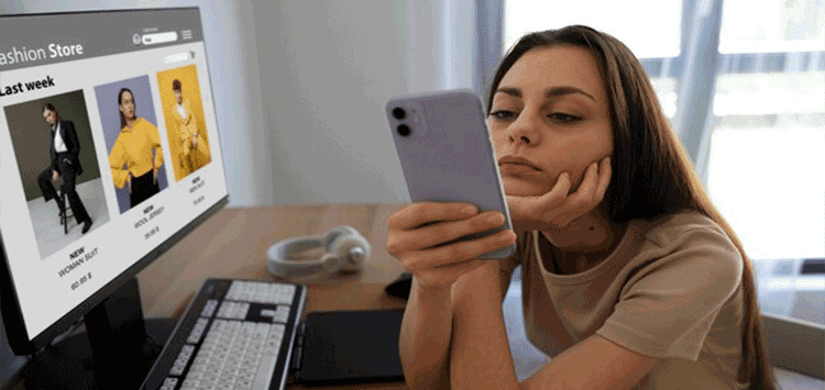 Uma mulher sentada em frente a um computador segurando um telefone celular