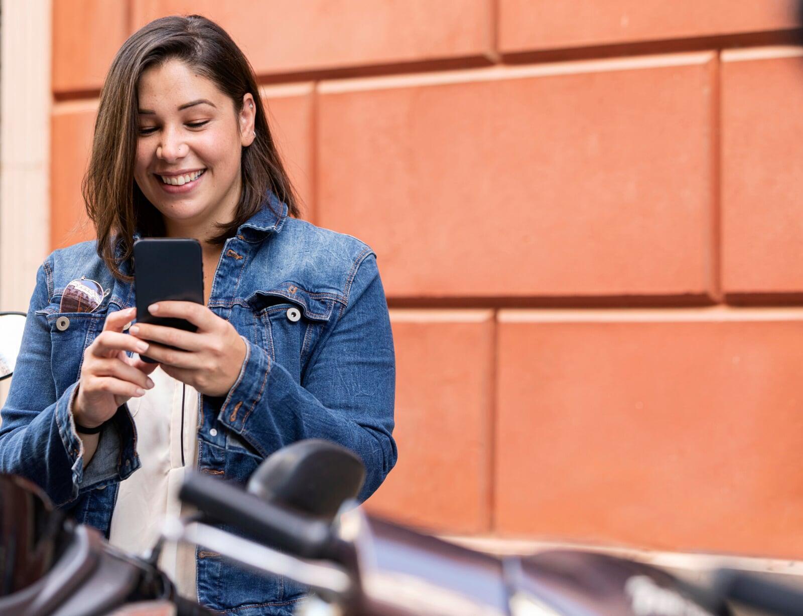 Mulher sorridente utilizando celular na rua, representando ações de marketing digital voltadas ao consumidor final