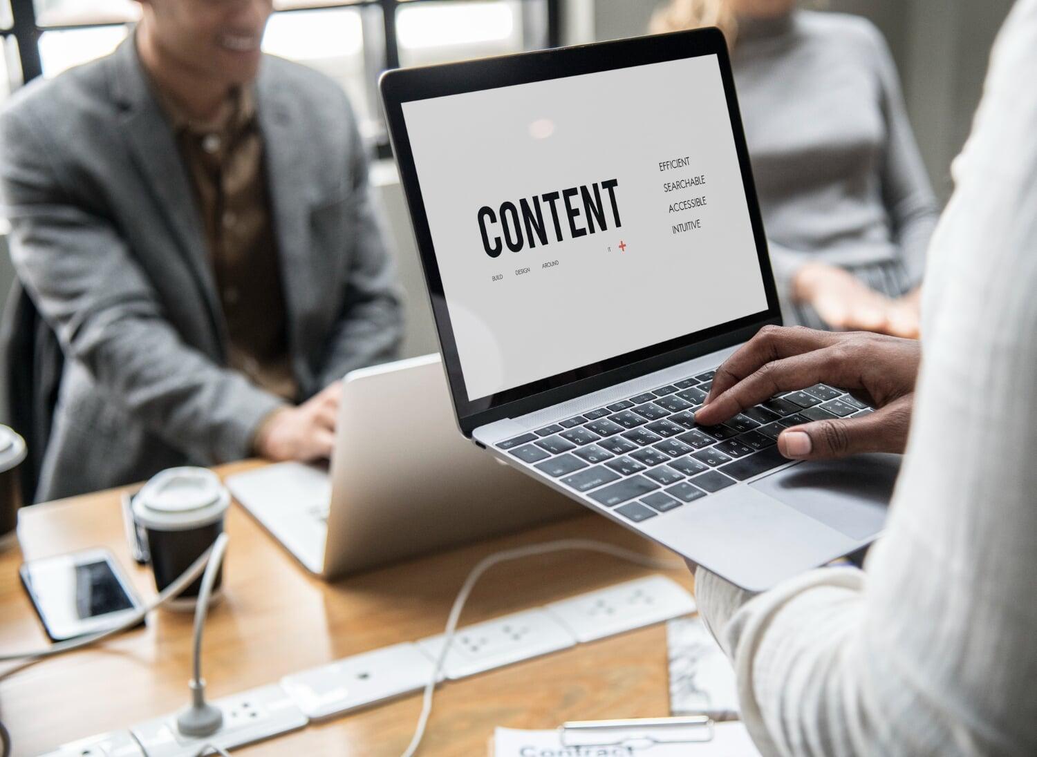 Pessoa segurando notebook com a palavra "Content" na tela durante reunião