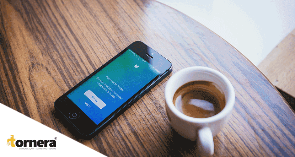 Uma xícara de café e um iphone com twitter aberto sobre uma mesa