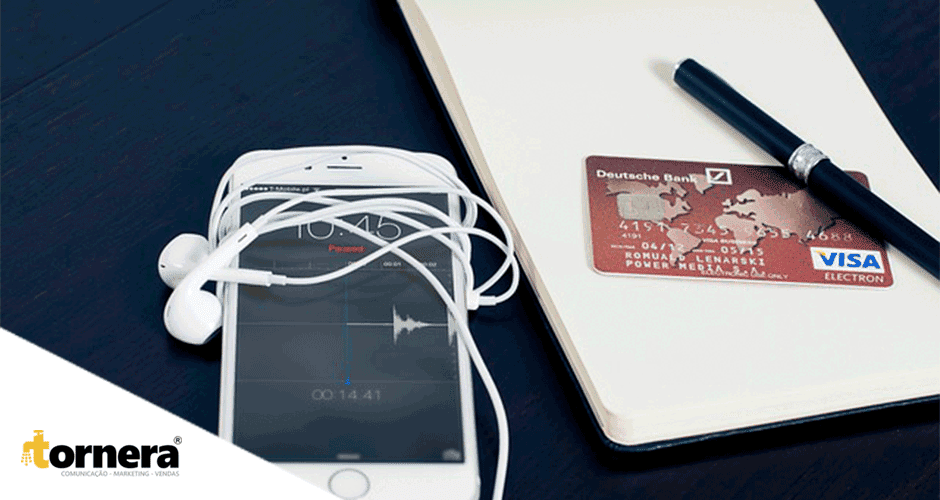Um telefone celular, fones de ouvido e um cartão de crédito sobre uma mesa